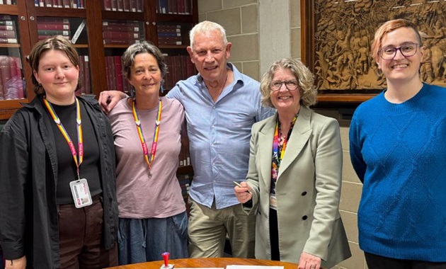 Five people stand in the library in front of bookshelves, smiling.