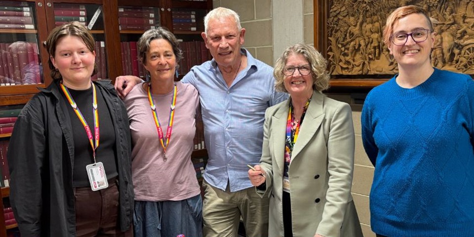 Five people stand in the library in front of bookshelves, smiling.
