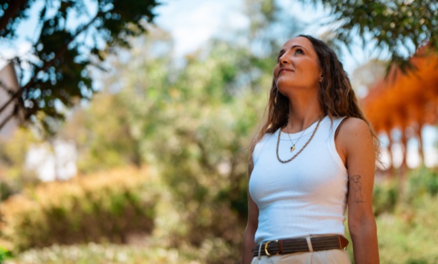 Woman in white singlet looks up at a tree on Murdoch University's bush campus