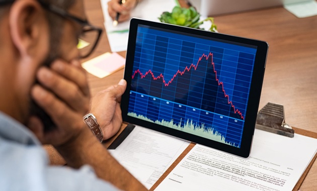 A person looking at a screen with a graph declining showing a stock market crash.