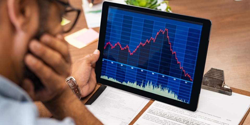 A person looking at a screen with a graph declining showing a stock market crash.