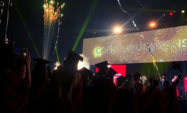 Graduates at ceremony with big Congratulations banner in background