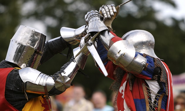 Two knights in medieval armour dueling with swords in the arena at a medieval festival