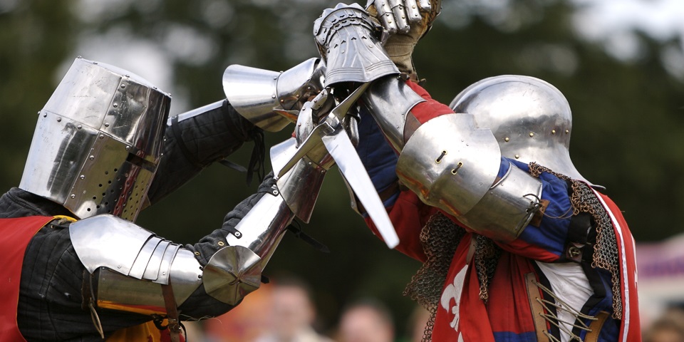 Two knights in medieval armour dueling with swords in the arena at a medieval festival