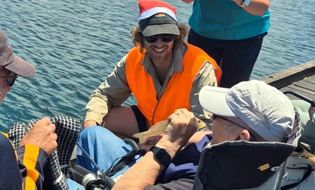 Kurt Krispyn sitting on the jetty by the water with two Fishability members.