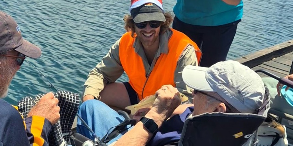 Kurt Krispyn sitting on the jetty by the water with two Fishability members.
