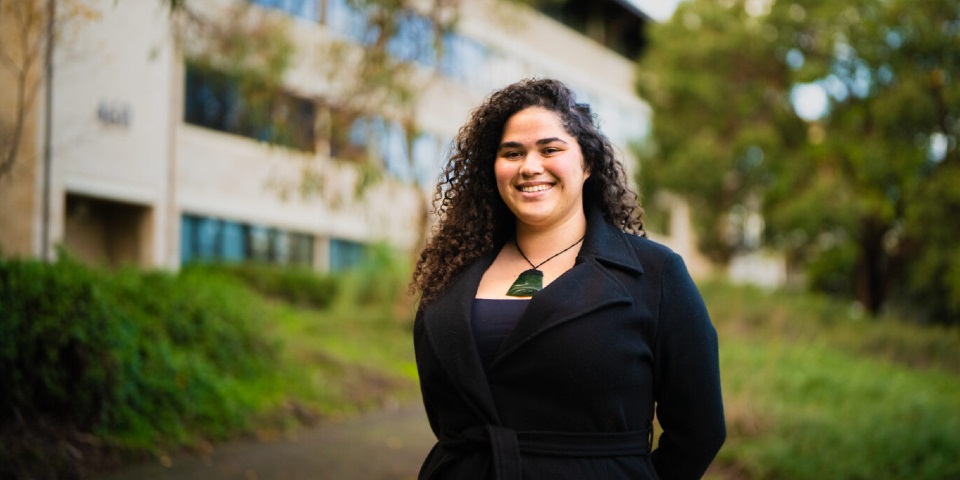 Aboriginal-Moari student standing in front of law building and gardens smiling at camera
