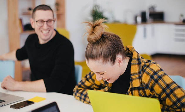 Woman and man laughing at desk with laptops