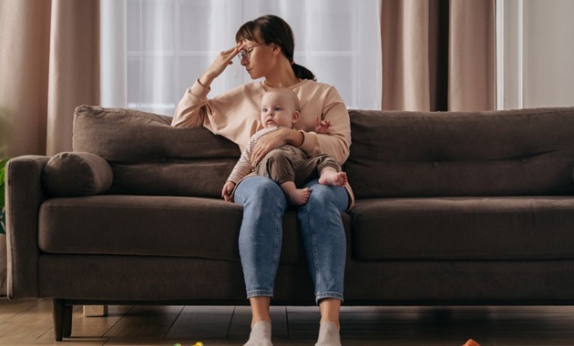 A mother looking distresses holding her baby on the couch.