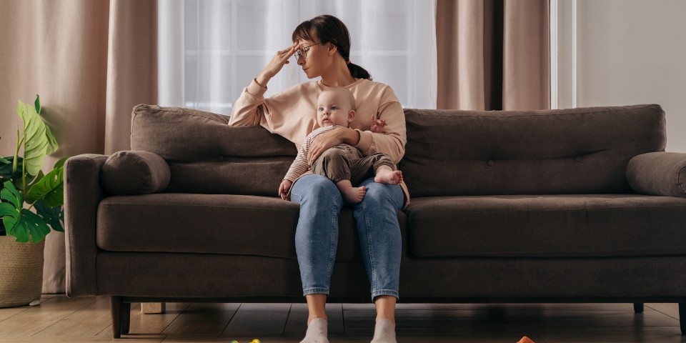 A mother looking distresses holding her baby on the couch.