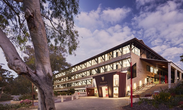 Murdoch University Chancellery Building at sunset with lights illuminating the inside.