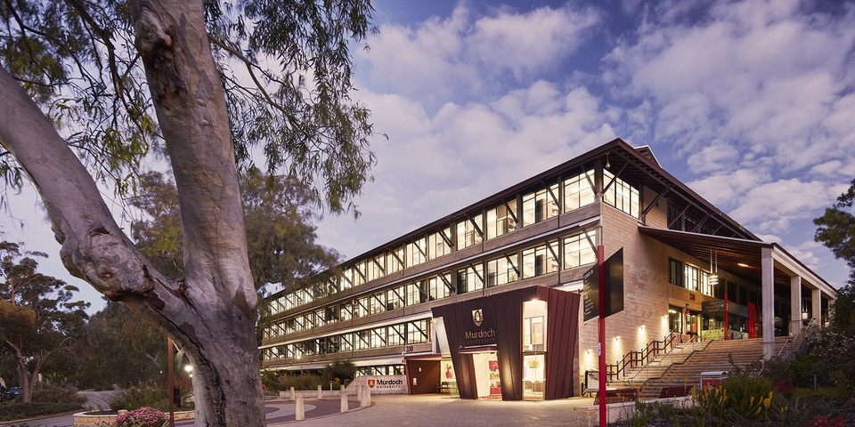 Murdoch University Chancellery Building at sunset with lights illuminating the inside.