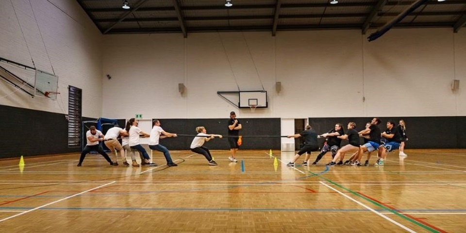 Two teams of people in a gym playing tug-o-war with a rope.
