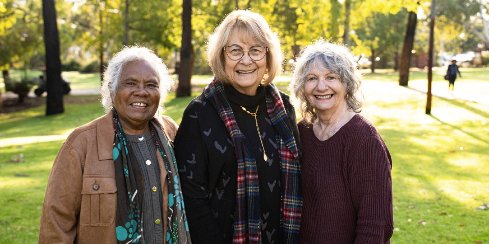Three women standing on grassed area smiling at camera