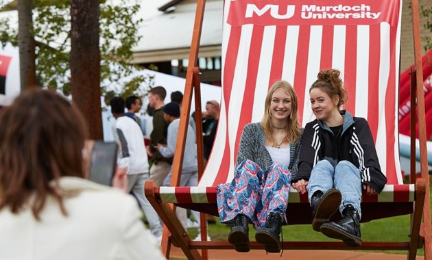 Two people sitting on a giant lawn chair smiling and laughing