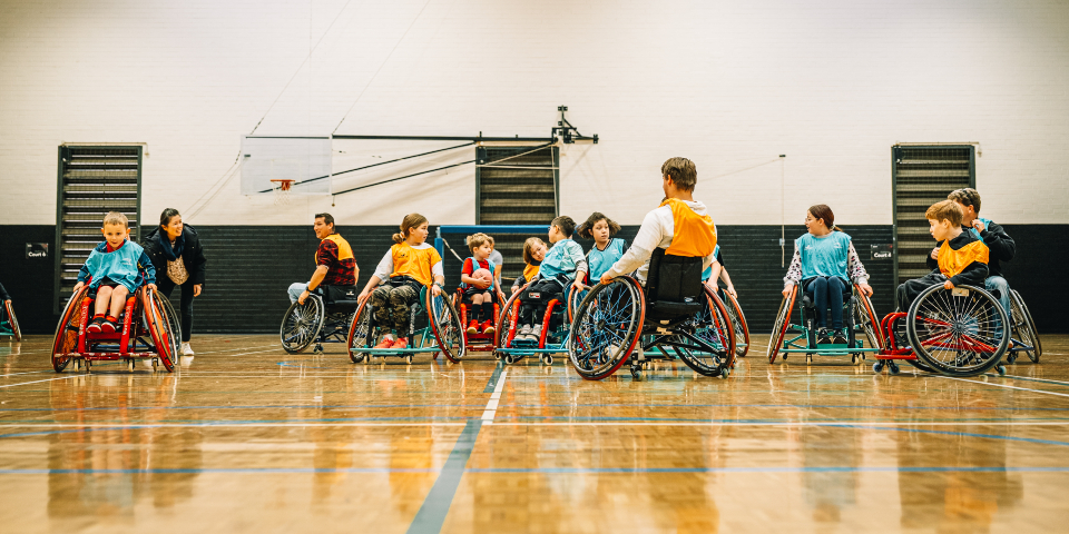 Young people in wheelchairs on gym court playing handball