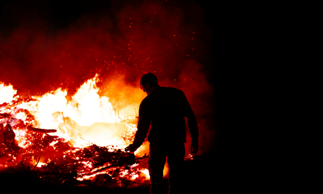 Silhouette of a man standing in front of a fire.