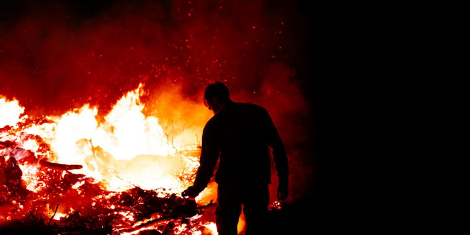 Silhouette of a man standing in front of a fire.