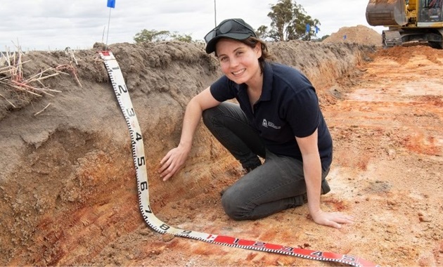 Soil scientist Jenni Clausen kneeling in dirt with a giant measuring tape