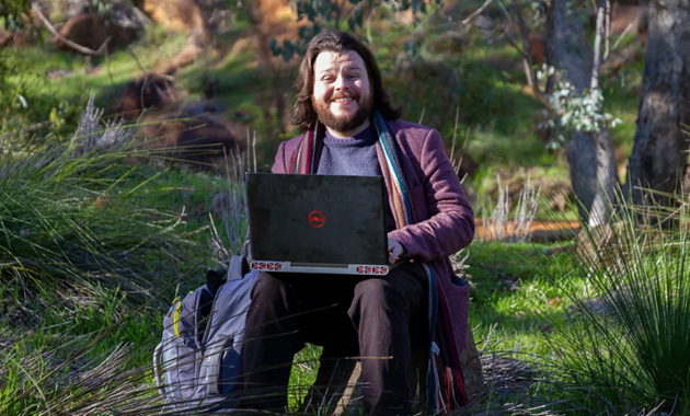 Stephen B Platt sitting amid greenery with a laptop on his lap.