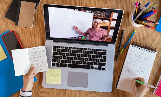 A student watching an online lecture and taking notes