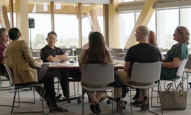 Group sits around a table, smiling.