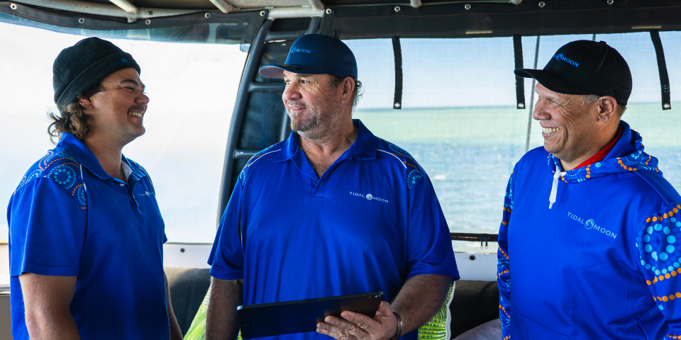 Tidal Moon crew Three men in blue shirts standing on a boat smiling at each other