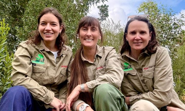 Three scientists crouching among a field of trees.