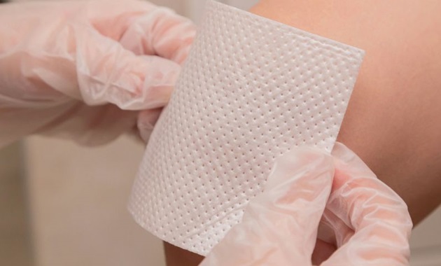 A pair of gloved hands putting a bandage on someone's arm.