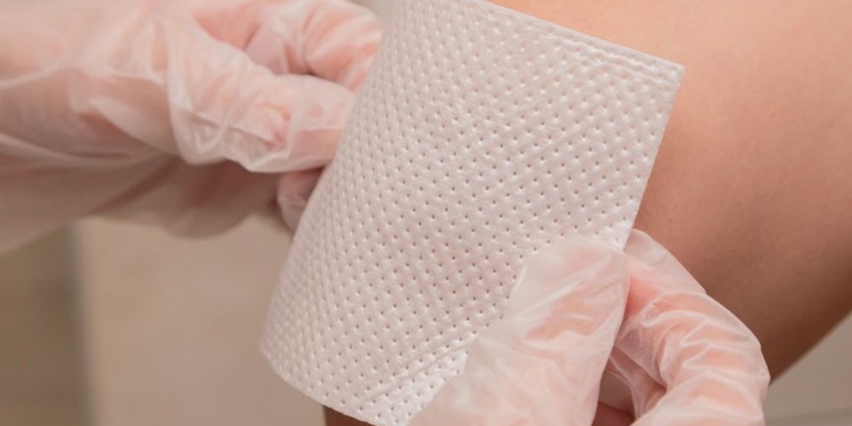 A pair of gloved hands putting a bandage on someone's arm.
