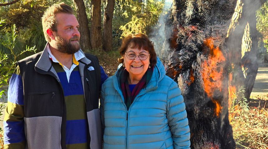 Rohan Collard and Professor Rhonda Marriott AM standing in front of a burning balga tree.
