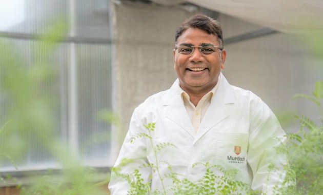 Professor Rajeev Varshney standing in a field wearing a lab quote and smiling.