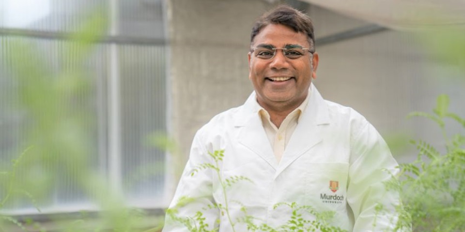 Professor Rajeev Varshney standing in a field wearing a lab quote and smiling.