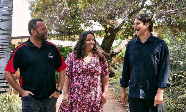 Three people standing in front of trees and bushland smiling.