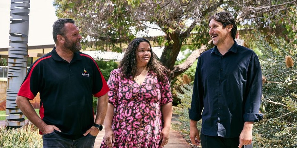 Three people standing in front of trees and bushland smiling.