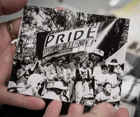 A photo from the WestPride Archives of a historical Pride march being held by a hand.