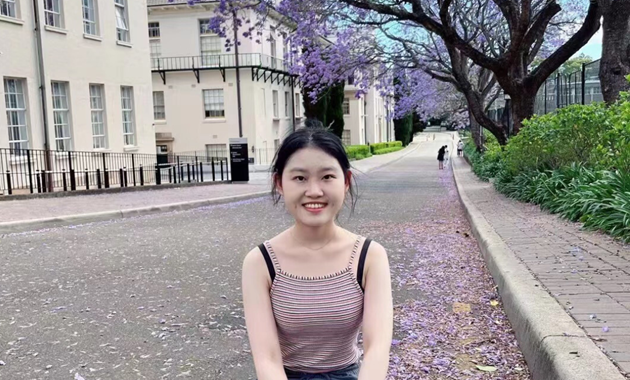 Dr Yunwei sitting in front of jacaranda trees