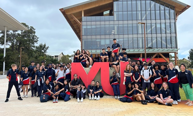 Students in uniform posing in front of the Murdoch University logo.