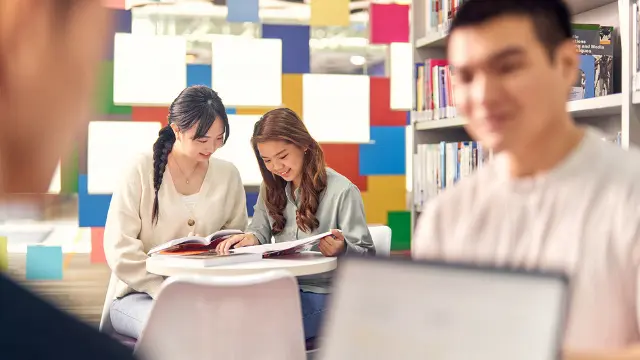 Blurred males in foreground and two females at study table in the background